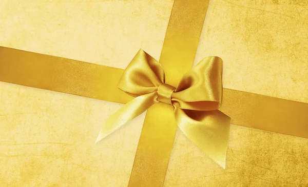 Shiny golden satin ribbon bow on gold background — Stock Photo, Image