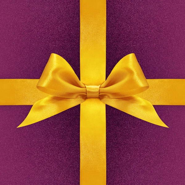 Блискучий золотий атласний стрічковий лук на фіолетовому фоні — стокове фото