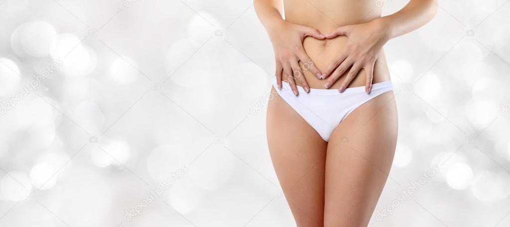 woman hands heart shape on belly, isolated on blurred lights bac