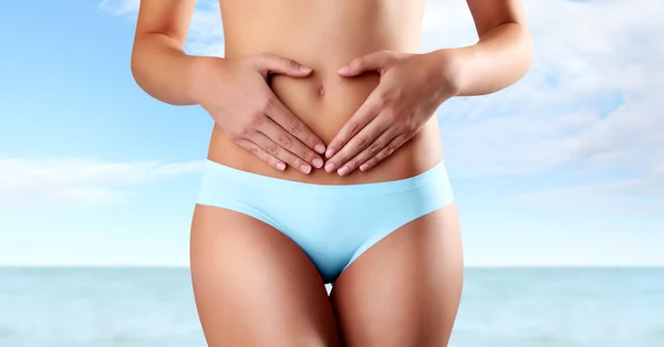 Mujer manos forma de corazón en el vientre, aislado en el cielo azul y el fondo del mar — Foto de Stock