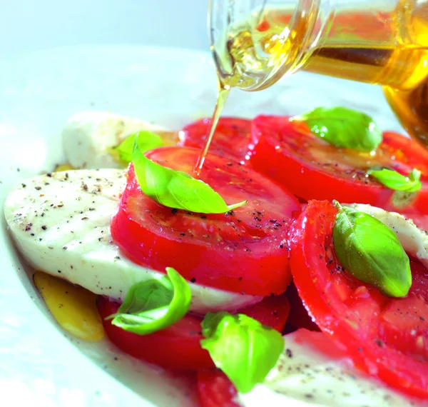 Derramando azeite sobre tomate e mussarela — Fotografia de Stock