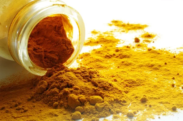 Ground turmeric spilling from glass jar — Stock Photo, Image