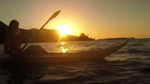 Zeitlupe: Junge Frau im Kajak auf dem Meer bei goldenem Sonnenuntergang — Stockvideo
