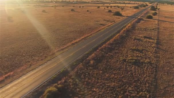 AERIAL: Carro preto do SUV que conduz ao longo da estrada rural vazia no por do sol dourado do verão — Vídeo de Stock