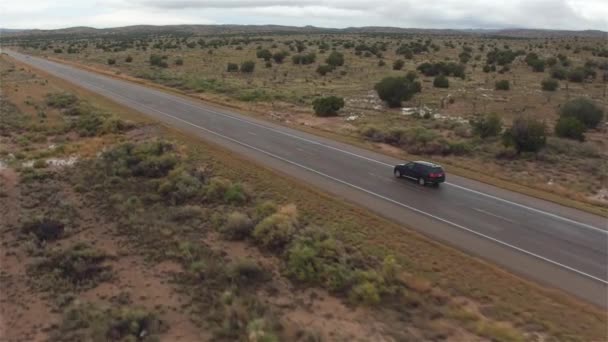 AERIAL: Carro preto SUV dirigindo na estrada rural vazia molhada em mau tempo chuvoso — Vídeo de Stock
