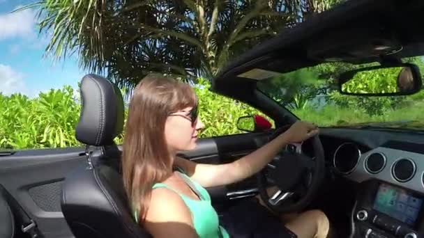 LOW MOTION: Jovem mulher em cabrio carro passando por árvores exóticas ao longo da praia — Vídeo de Stock