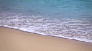 SLOW MOTION CLOSE UP: Turquoise ocean wave foam washing white sandy beach
