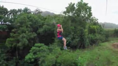 Young girl having fun while riding zipline cable above beautiful green jungle