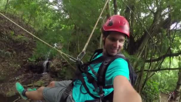 Glad leende ung man glider på zipline i vackra frodiga djungel regnskog — Stockvideo