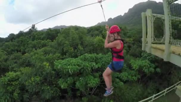 Молода дівчина посміхається і кричить, коли застібається на кабель над пишними тропічними лісами — стокове відео