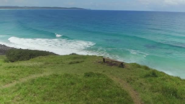 Antenn: Tom bänk ovanför vackra vulkaniska kusten och smaragdgröna havet — Stockvideo