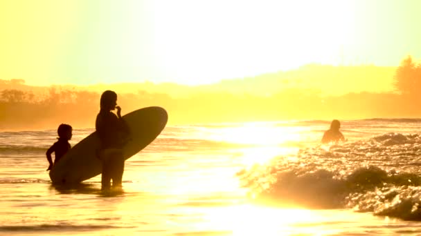 SLOW MOTION: Mother and daughter observing waves in shallow water with surfboard — Stock Video