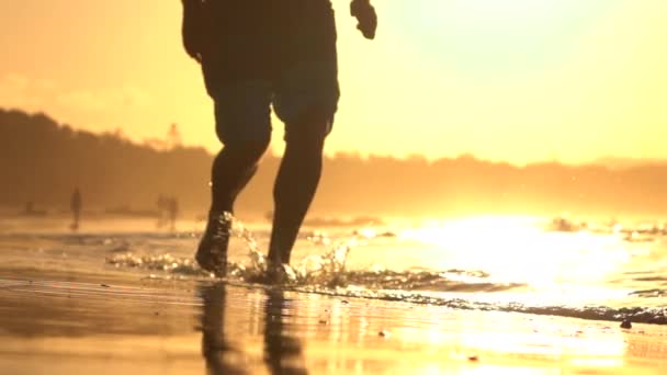 クローズ アップ: 若い選手男黄金の夕日で浅い海の水を実行します。 — ストック動画