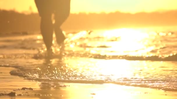 Z bliska Dof: Młody człowiek jogging w wodzie płytkiej ocean o wspaniałe pomarańczowy zachód słońca — Wideo stockowe