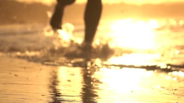 スローモーション: 若い男が見事なオレンジ色の夕日に浅い海の水でジョギング — ストック動画