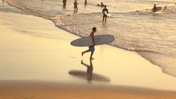 Счастливый юный серфер с доской для серфинга в руках бежит в океан — стоковое видео
