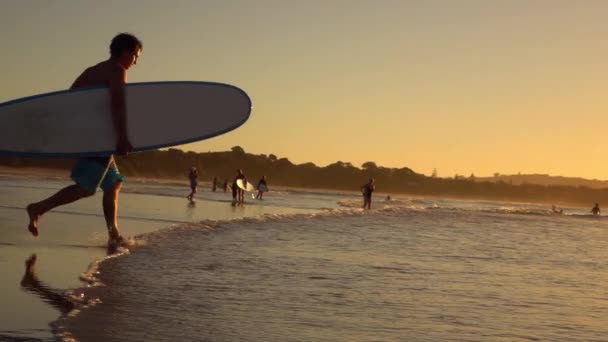 Slow Motion: Glada unga surfare kör med longboard i händer i havet — Stockvideo