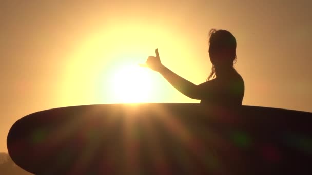 Närbild: Ung flicka surfare håller longboard, gör surfare shaka tecken gest — Stockvideo