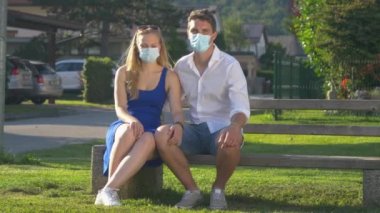 Parktaki bankta otururken maske takan ve öpüşen çiftler.