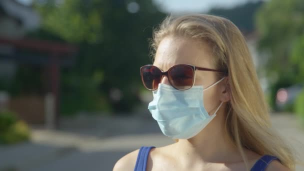 FERMER : Une jeune femme caucasienne porte des lunettes de soleil et un masque chirurgical bleu clair. — Video