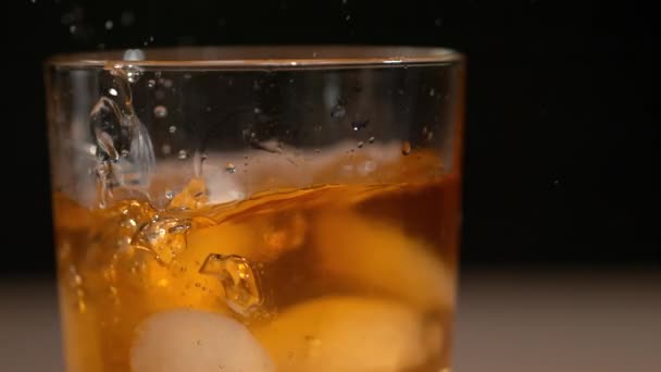 Круглые кусочки льда падают в элегантный стакан, полный вкусного бурбона. — стоковое видео