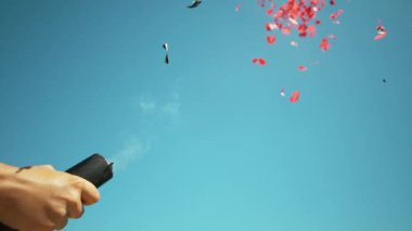 Tanımlanamayan kişi açık mavi gökyüzüne konfeti tabancasıyla ateş ediyor..