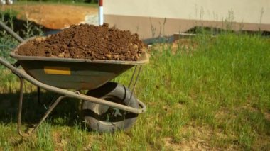 Islak toprak dolu büyük metal el arabası arka bahçeye itiliyor..