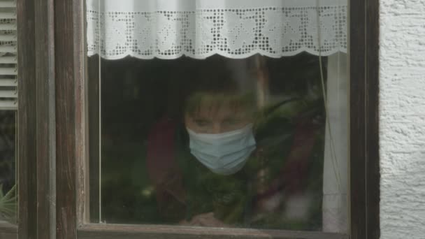 Yüz maskesi takan bunalımlı yaşlı kadın pencereden dışarı bakıyor.. — Stok video