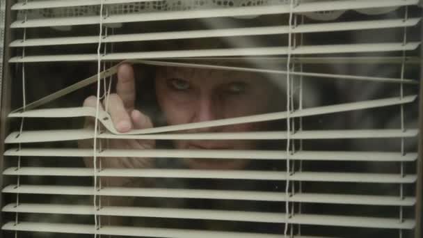 CLOSE UP: Scared woman looks out her window while being locked down during virus — Stock Video