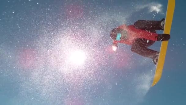 BOTTOM UP: Flocos de neve brilham ao sol enquanto o piloto faz truques de snowboard. — Vídeo de Stock