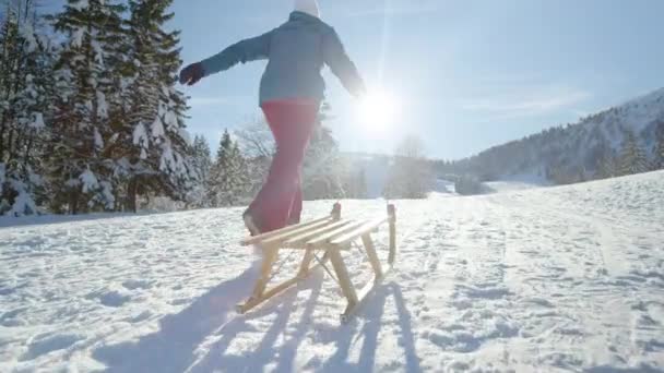 Oigenkännlig ung kvinna springer längs en snöig äng och drar sin släde. — Stockvideo