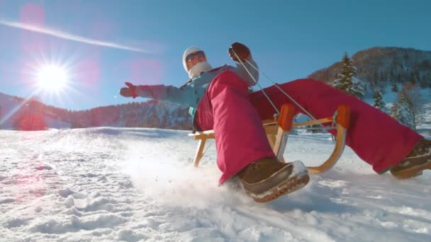 レンズフレア:幸せな白人女性が木製のそりで雪の丘をスピードダウン. — ストック動画