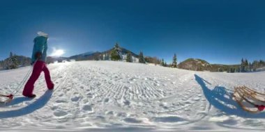 VR360: Genç bayan turist yokuş yukarı yürüyor ve arkasından ahşap bir kızak çekiyor.