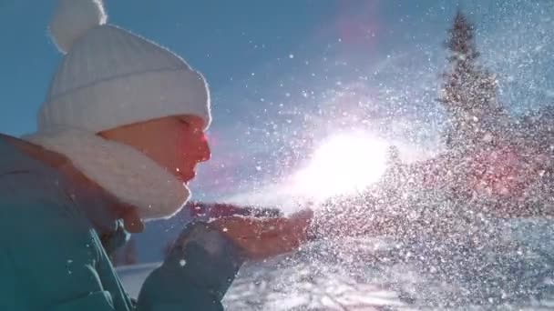 STÄNGA UPP: Snöflingor glittrar i solsken när kvinnan blåser i handen full av snö — Stockvideo