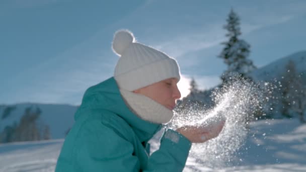 Ung kvinna blåser i handen full av snö och vänder sig mot kameran.. — Stockvideo