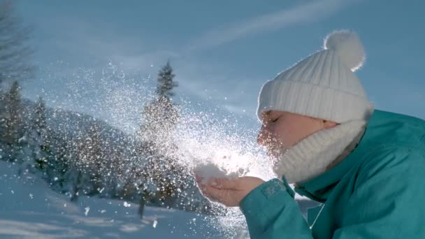 CLOSE UP: Lekfull kvinnlig turist blåser snöflingor i vintersolen. — Stockvideo