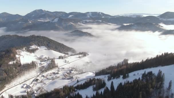 AERIAL: Pequeño pueblo en los serenos Alpes Julianos en una nebulosa mañana de invierno. — Vídeos de Stock