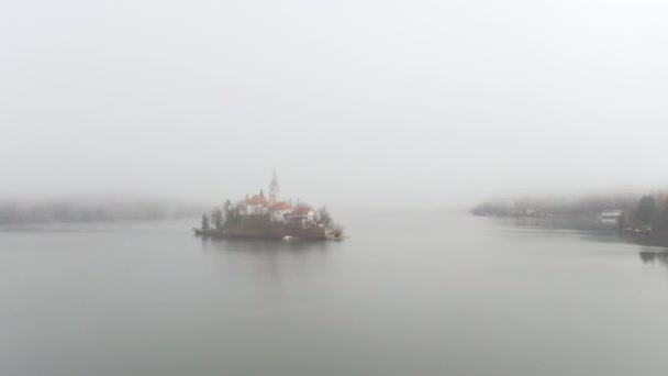 AERIAL: Idyllische Insel inmitten des Bleder Sees ist von dichtem Nebel umgeben. — Stockvideo