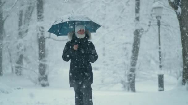 CLOSE UP: Ung kvinna i tjock vinterrock promenader längs avenyn under en snöstorm — Stockvideo