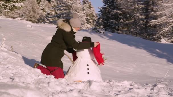 FECHAR UP: Mulher coloca um lenço vermelho e nariz de cenoura no boneco de neve que ela está construindo — Vídeo de Stock