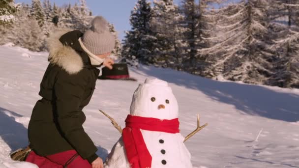 PORTRAIT: Gelukkige vrouw lacht na het zetten van een zwarte hoed op een grappige sneeuwpop. — Stockvideo