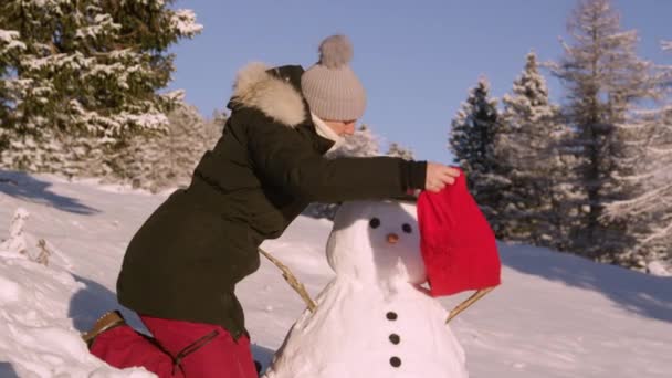 FECHAR UP: Jovem mulher se divertindo na neve coloca um lenço em torno do pescoço do boneco de neve. — Vídeo de Stock