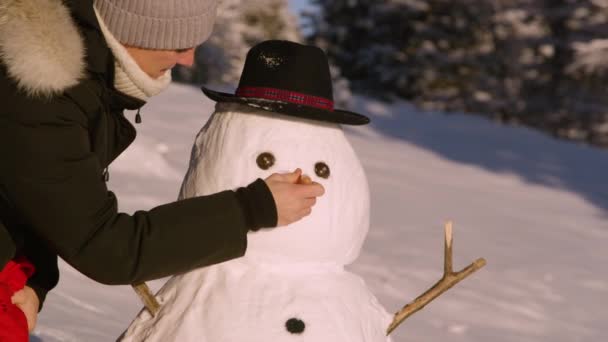 CHIUDI: Donna giocosa mette un naso di carota e una sciarpa rossa sul simpatico pupazzo di neve. — Video Stock