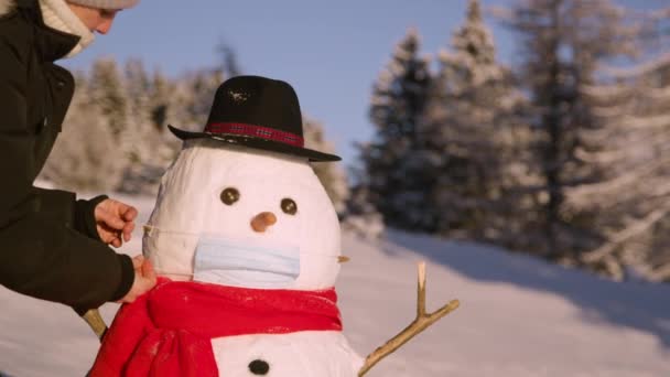 CLOSE UP: Young Caucasian woman puts a surgical mask on the funny snowman. — Stock Video