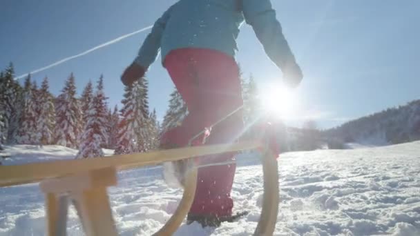 Nízký úhel: Nerozpoznatelná žena běží na zasněžený kopec se svými dřevěnými saněmi. — Stock video