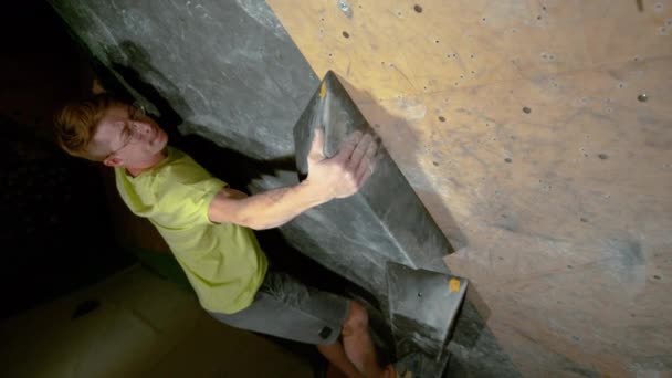 CLOSE UP: Atletische jongeman grijpt een zwart volume hold tijdens het boulderen binnen. — Stockvideo