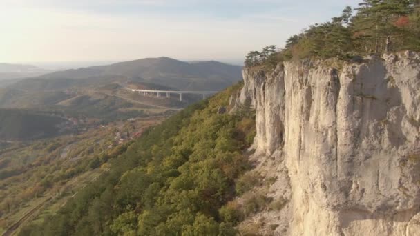 AERIAL: Lecąc obok górującego urwiska z widokiem na jesienny kolorowy krajobraz. — Wideo stockowe