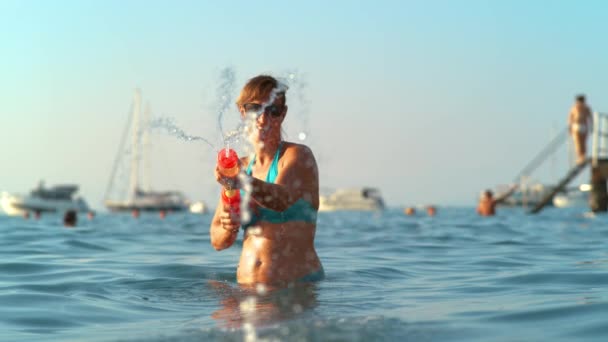 PORTRAIT: Smiling young woman enjoying her summer vacation shoots a water gun. — Stock Video
