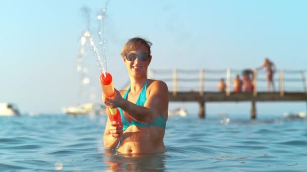 PORTRAIT: Fit tourist squirting water with a plastic toy gun while at the beach. — Stock Video