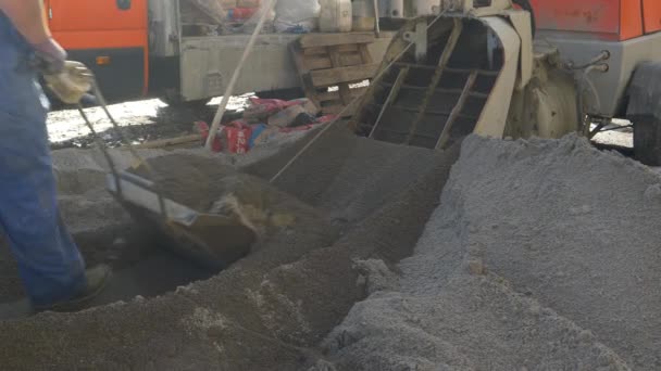 CLOSE UP: Male worker pushes a scoop of black screed sand towards a machine. — Stock Video